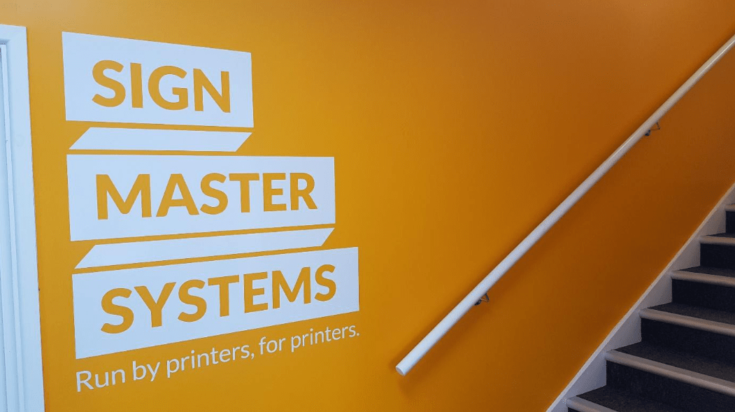 The Signmaster logo as an example of a retail wall graphic on one of their orange office walls