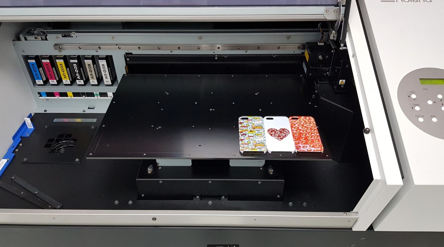A UV printers with three different phones on top of it, ready to be printed upon.